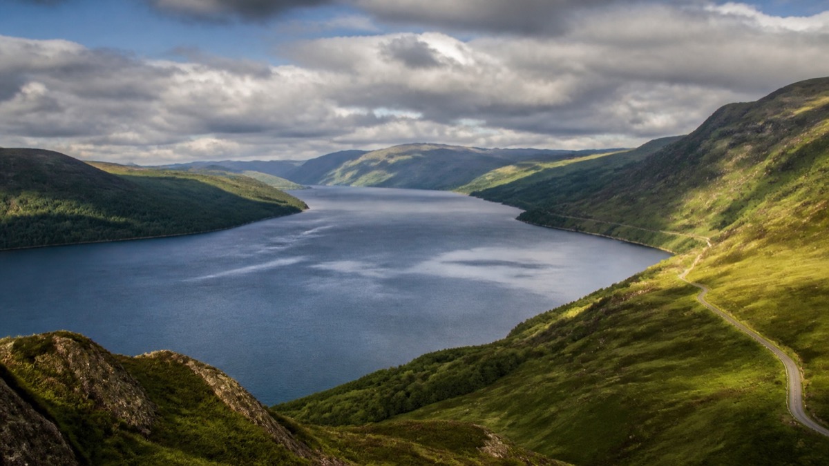 Loch Ness surrounded by green mountains beneath dramatic Highland clouds