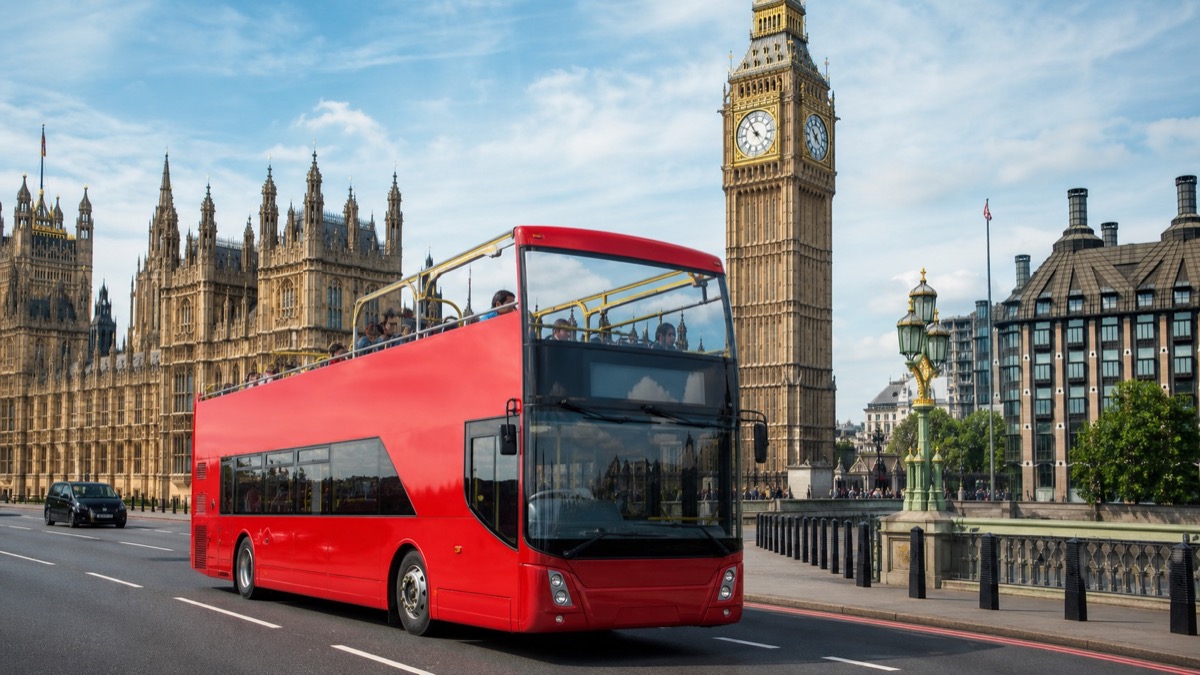 Red open-top sightseeing bus travelling past the Elizabeth Tower in London